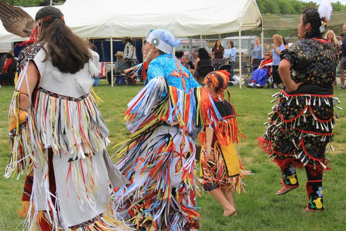 Group of people in colorful traditional Native American dance attire performing outdoors.