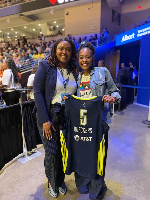 Two women smiling, holding a basketball jersey.