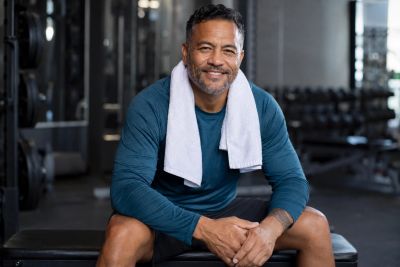Smiling man with towel around neck resting on gym bench.