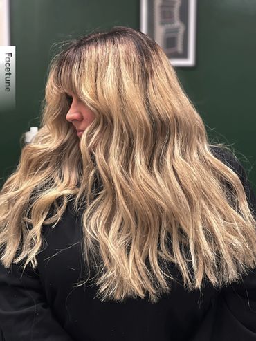 Woman with long, wavy blonde hair and bangs in a black top.