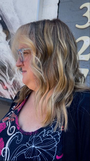 Side profile of a woman with wavy blonde and brown hair wearing glasses.