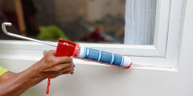 A person applies sealant around a window frame using a caulking gun.