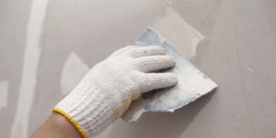 Hand with glove smoothing wall plaster with a metal trowel.