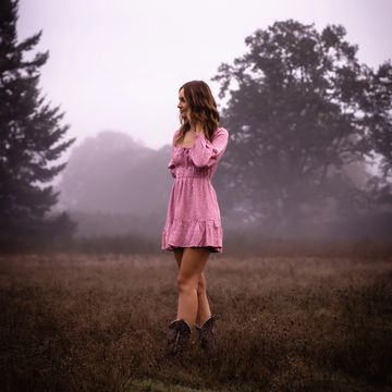 A woman in a pink dress stands in a misty field.