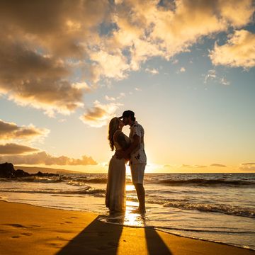 Couple embracing at sunset on the beach, casting long shadows.