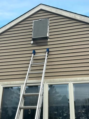 Ladder leaning against house below small attic window.