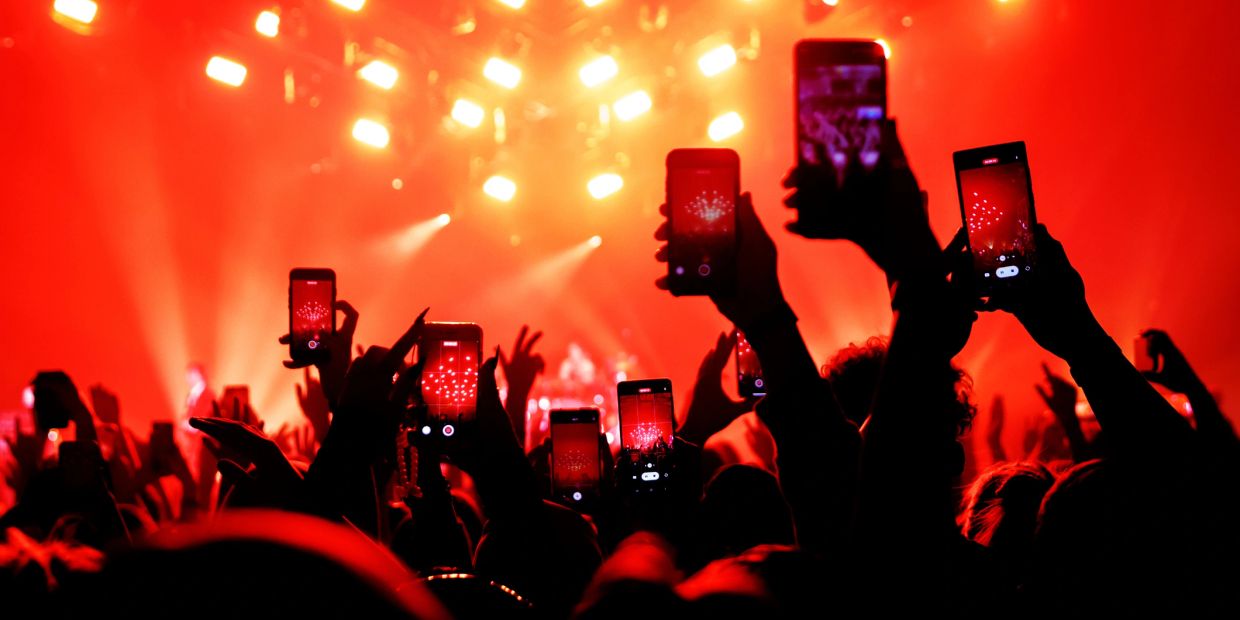 Audience captures a vibrant concert with phones amid red lighting.