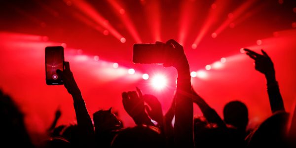 Crowd capturing a vibrant concert with phones held high under red stage lights.