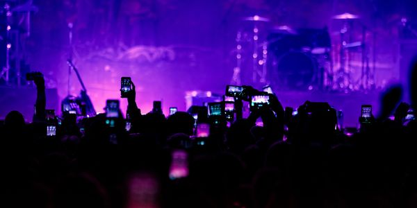 Audience capturing a live concert with phones under purple stage lights.