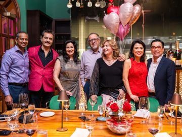 Group of well-dressed friends posing at a festive table with balloons and wine glasses.