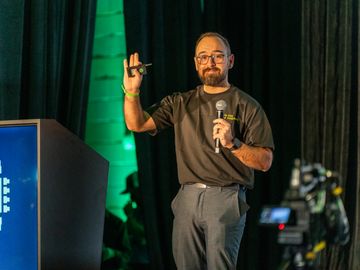 Speaker presenting on stage at a conference with a microphone and remote.