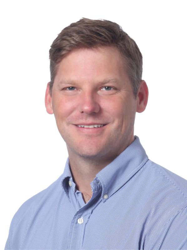 Smiling man in a light blue button-up shirt against a white background.