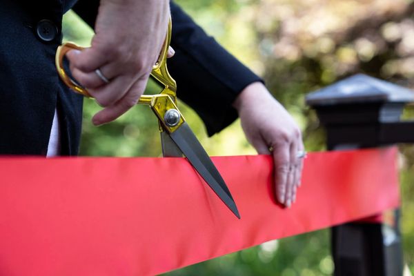 A pair of scissors cutting a red ribbon for a ceremony