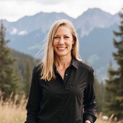 Smiling woman in black shirt standing outdoors with mountains in background.