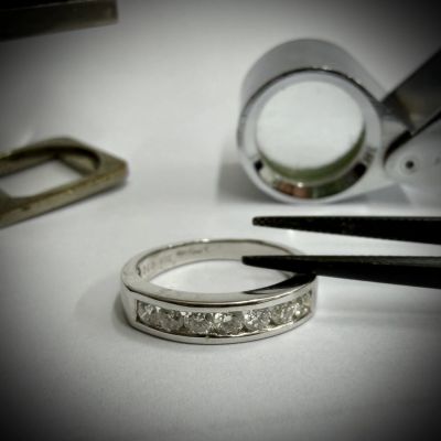Close-up of diamond ring being inspected with tweezers and a jeweler's loupe.