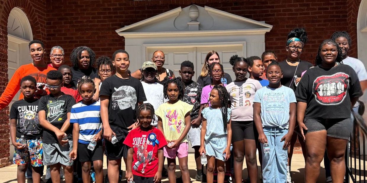 Group photo of kids and adults in front of a building on a sunny day.