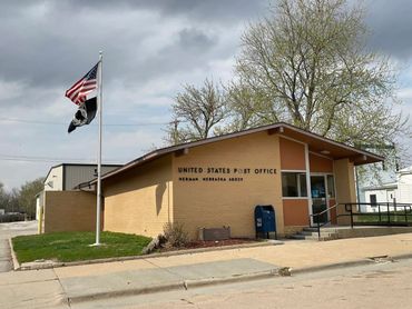 Small United States Post Office building in Herman, Nebraska with flags flying outside.