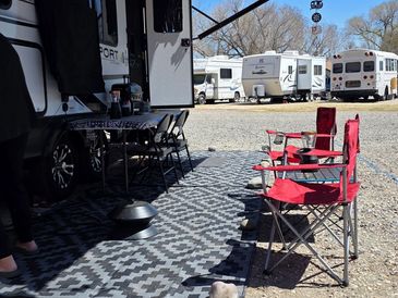 Outdoor camping setup with chairs, RV, and a sunny day under an awning.