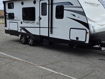 A white Passport travel trailer parked on a gray asphalt surface under a cloudy sky.