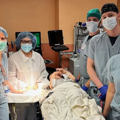 A photo of a woman with MSS laying on a hospital bed surrounded by people wearing surgical attire.