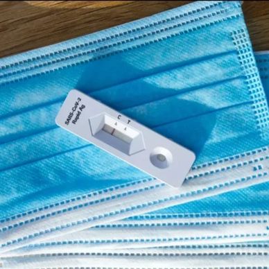 An image of a home Covid test laying on top of blue medical masks.