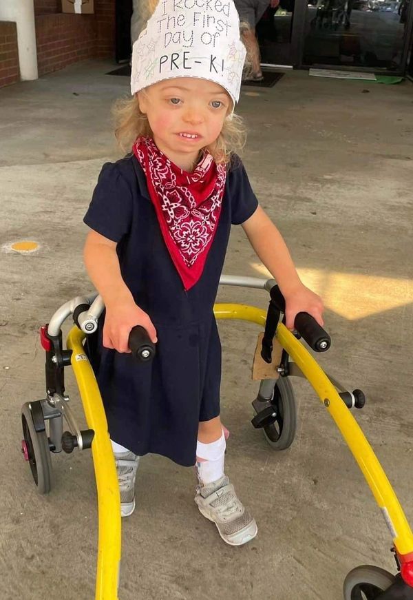 A young girl with MSS stands with her yellow walker outside of school on her first day of Pre-K.