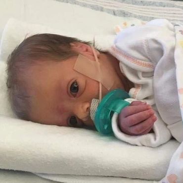 A newborn with MSS lays on her side in a hospital bed. She is sucking a pacifier.