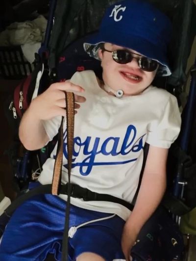A young man with MSS smiles while wearing a Kansas City Royals jersey and bucket hat.