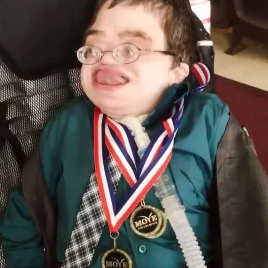 A young adult man with MSS smiles while wearing three medals around his neck.