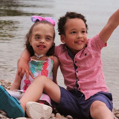 A girl with MSS and her brother sit together on a rocky beach.