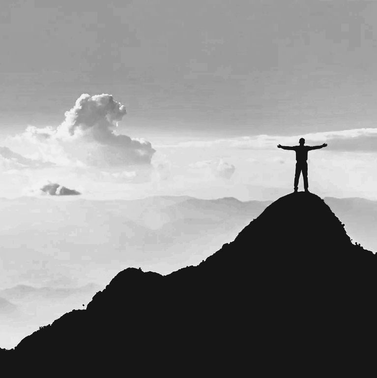 Silhouette of a person standing triumphantly on a mountain peak with arms outstretched.