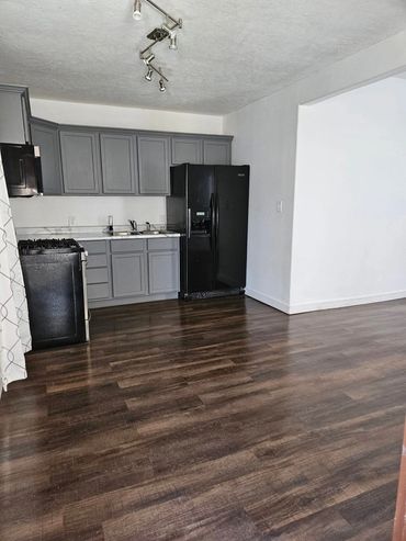 Modern kitchen with gray cabinets, black appliances, and dark wood flooring.