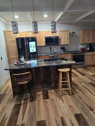 Modern kitchen with wooden cabinets and island, featuring pendant lights and two stools.