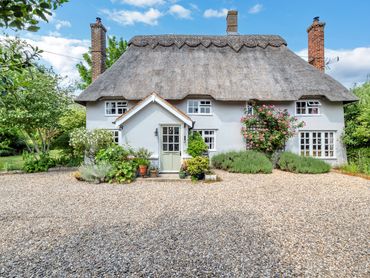 Traditional Suffolk thatched cottage with gravel driveway and mature cottage gardens