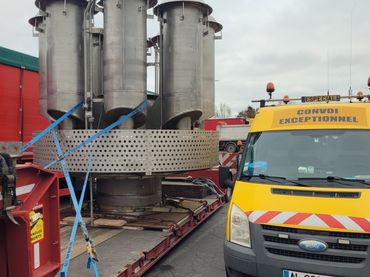 A yellow escort vehicle next to a heavy load on a trailer labeled 'Convoi Exceptionnel'.
