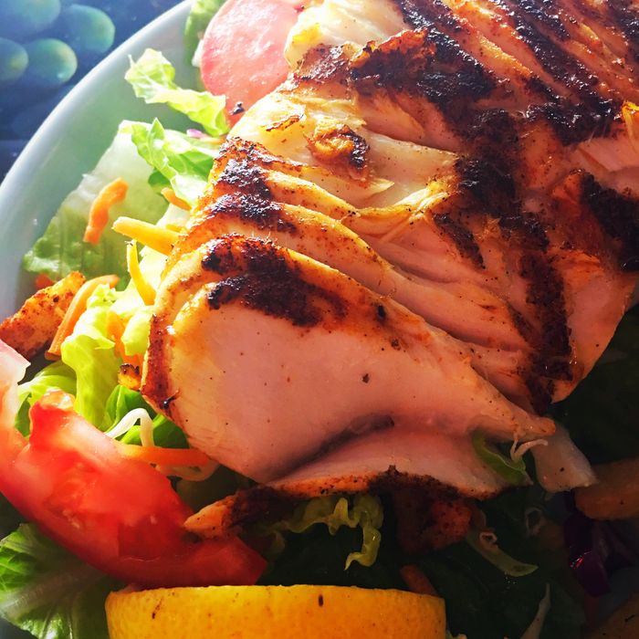 Grilled Halibut on a green salad with tomatoes and a fresh lemon slice
