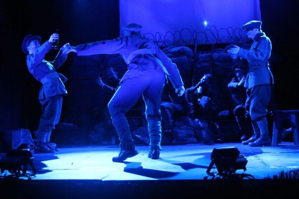 Lit only by blue light, 6 first world war soldiers dance in a trench scene on stage