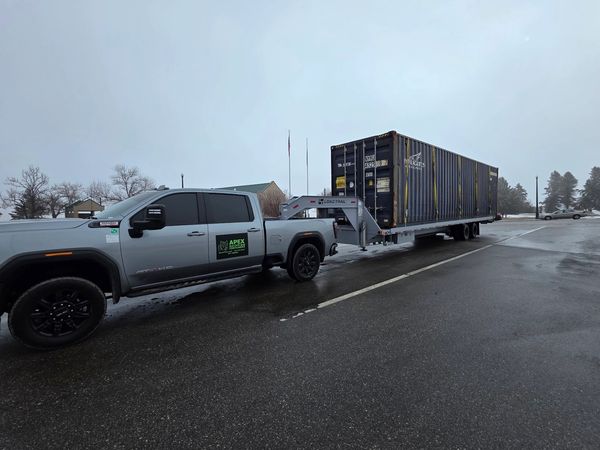 newer Gmc 1 ton pick up truck pulling a used 40ft Conex box on a tilt bed trailer in the snow in MN