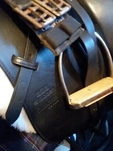 Close-up of a black leather saddle with metal stirrups and straps.