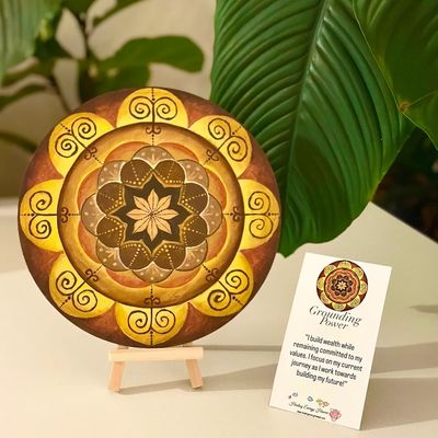 Decorative mandala with a positive affirmation card on a table with green leaves.