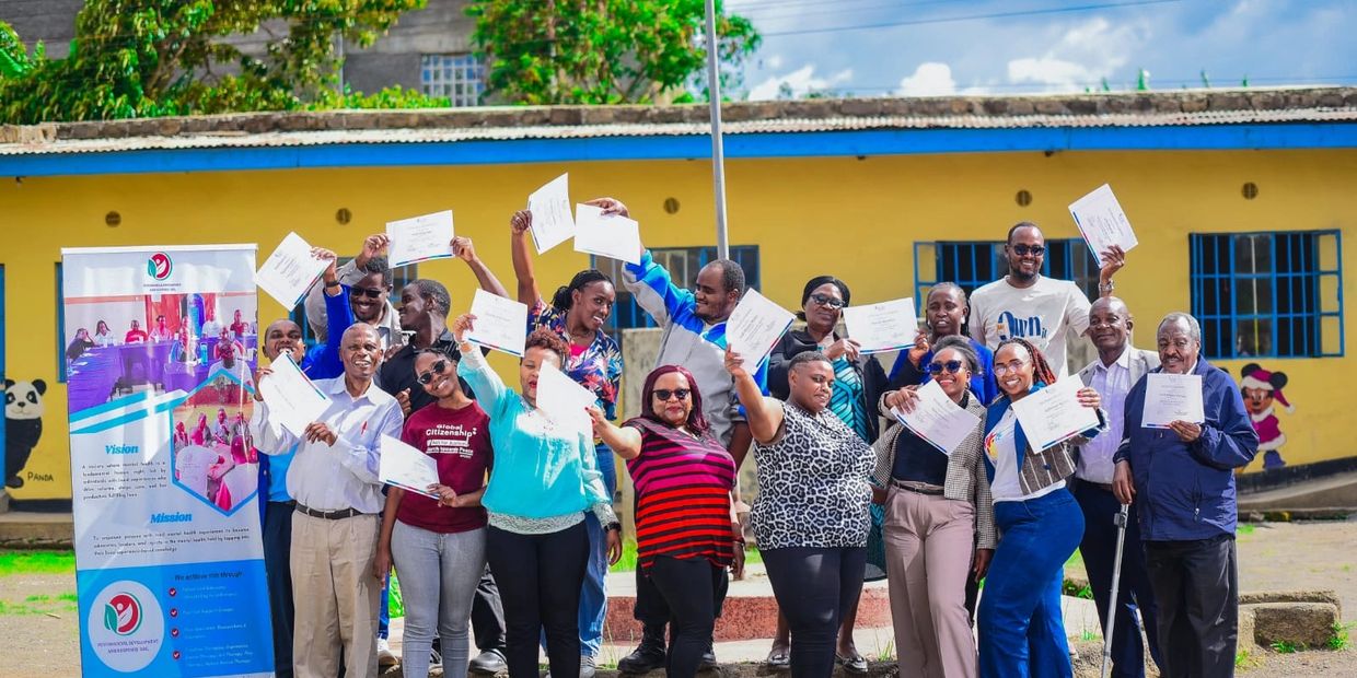 Group of people proudly holding certificates outdoors in front of a yellow building.