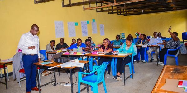A group of adults in a classroom setting with a presenter standing near a projector.