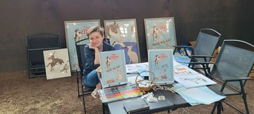 Angel King at a table with illustrated book displays and Just Keep Zippin' books.