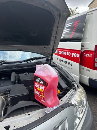 A container of Nulon coolant placed on a car engine with a service van in the background.
