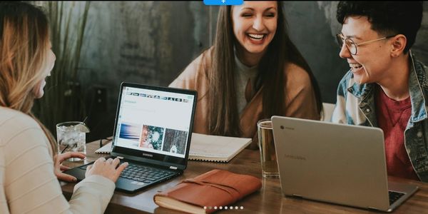 Three friends laughing and working together on laptops in a cozy setting.
