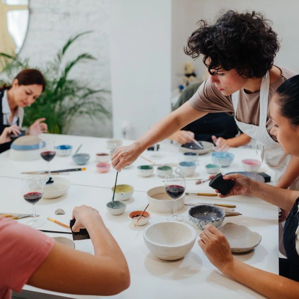 People painting pottery together at a creative workshop with wine glasses nearby.