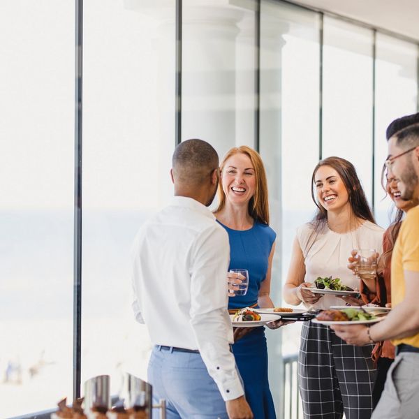 A group of colleagues smiling and chatting while holding plates of food and drinks.
