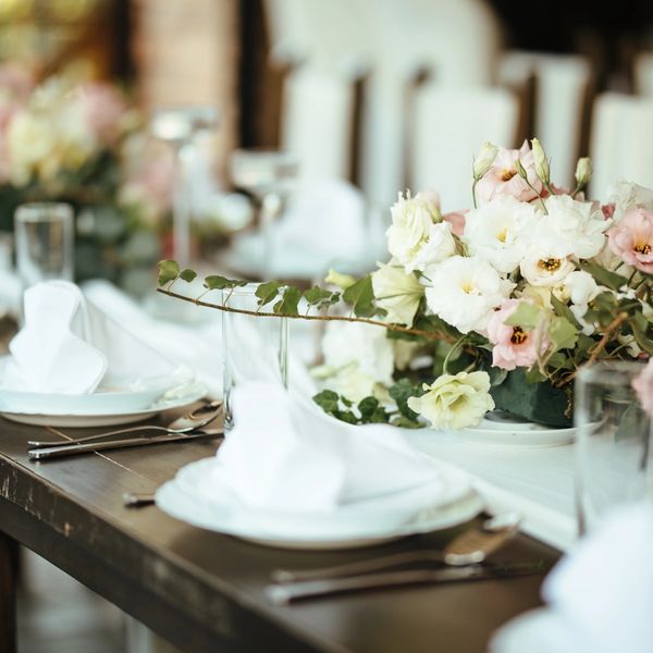 Elegant table setting with white and pink flowers and neatly arranged plates and cutlery.