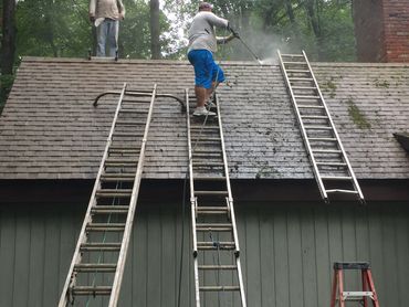 Man power washing a roof while another watches from the top.