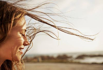 Close-up of a smiling woman with windblown hair outdoors.